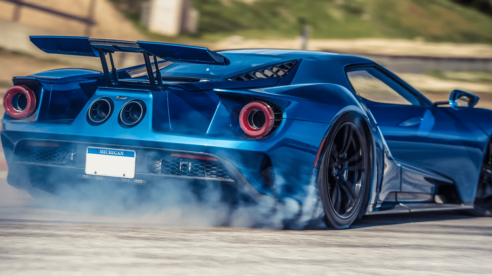 Blue 2017 Ford GT rear three-quarter view in Liquid Blue with tire smoke and red-accented taillights on a paved surface with Michigan plates